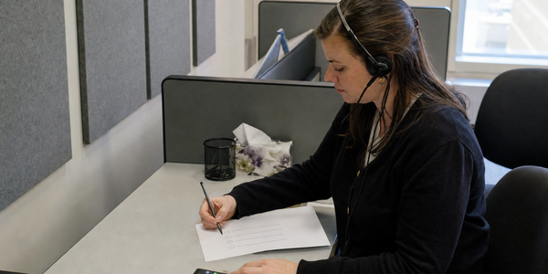 A polling interviewer listens through a wired headset while marking an unbranded response sheet.