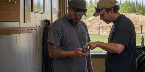 Two shooters check an unreadable phone together in a quiet range clubhouse.