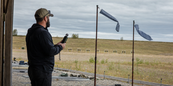A fictional range coach watches two wind flags at an unnamed Canadian long-range firing point.