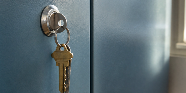 A cabinet key in a steel locker lock shares a small ring with two hanging brass house keys.