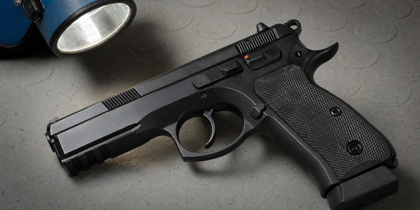 Illustrative unbranded handgun resting on a grey support under a blue inspection lamp.