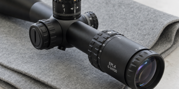 Close view of a black scope's rear glass, ribbed magnification ring and narrow tube on a grey work mat.