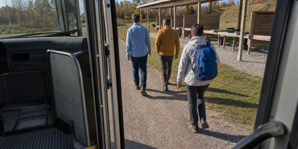 Generated illustration viewed from inside a bus doorway as adult newcomers approach an outdoor shooting-range shelter.