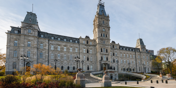 Illustrative view of Quebec’s Hôtel du Parlement, with its central clock tower, stone wings and curved public entrance.