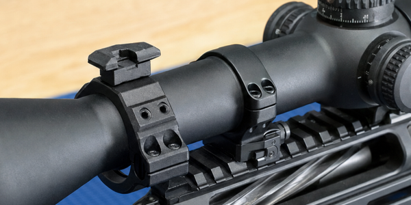 A small accessory collar and short rail sit on a scope tube ahead of its separate main support ring on a supported chassis rifle.