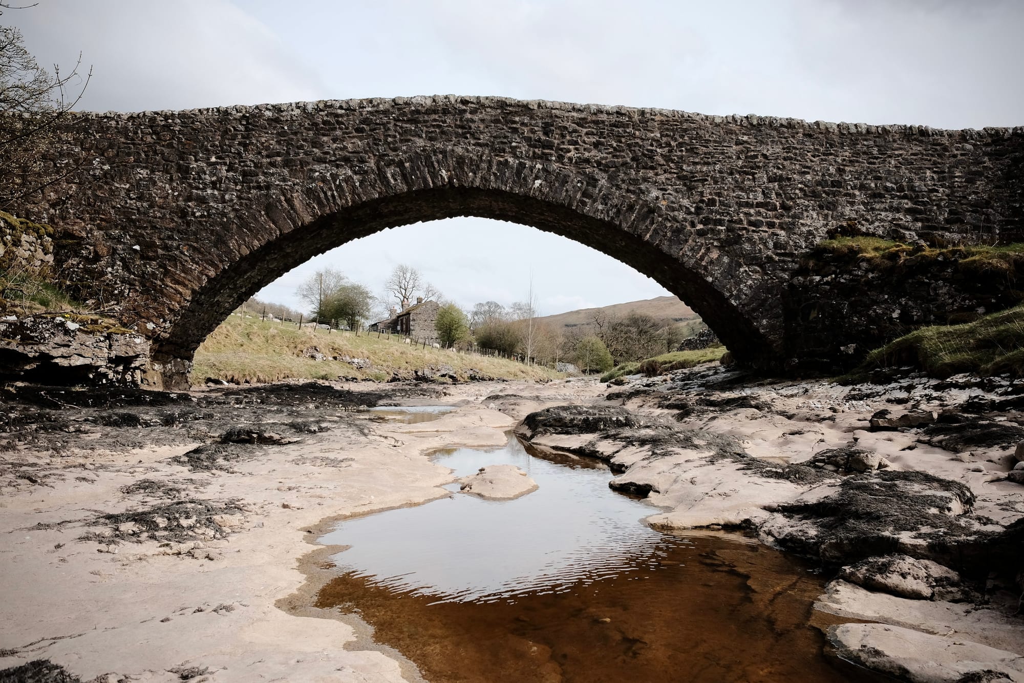 A stone bridge spans the rocky bed of a river with just a puddle of water in it.