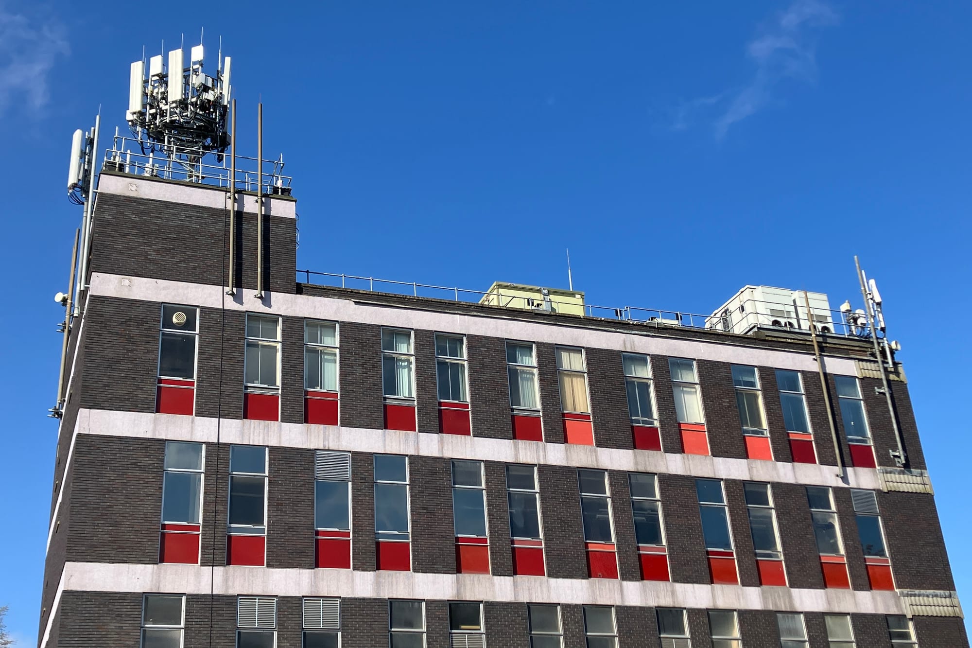 A dark brick building with bright red panels under its windows stands against a deep blue sky.