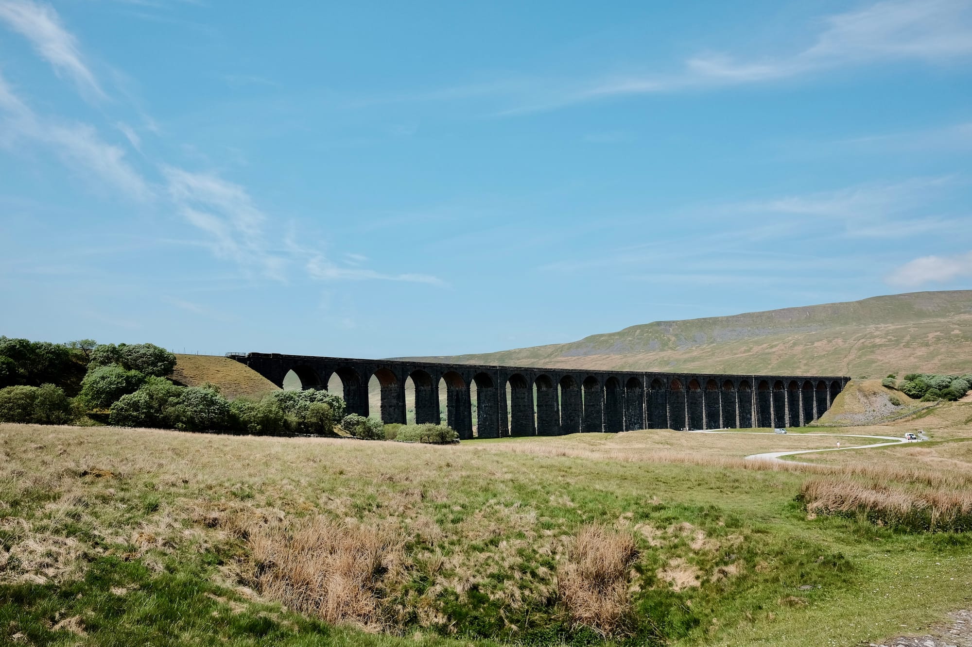 The dark structure of Ribblehead Viaduct stretches across a green valley in the Yorkshire Dales.