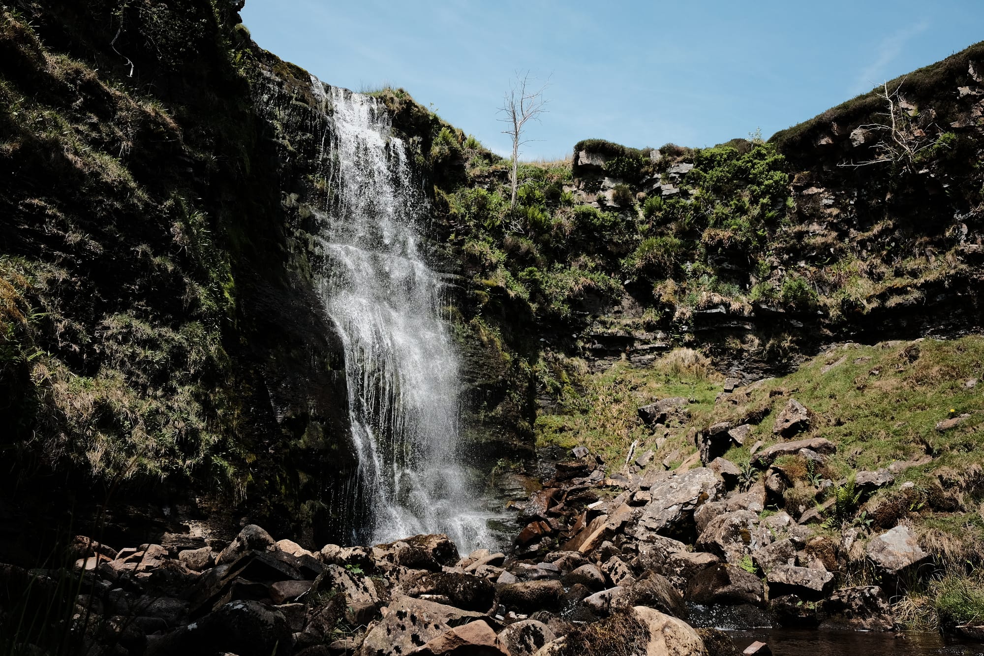 The Force Gill waterfall tumbles down a rock-and-grass cliff into a rocky gorge below.