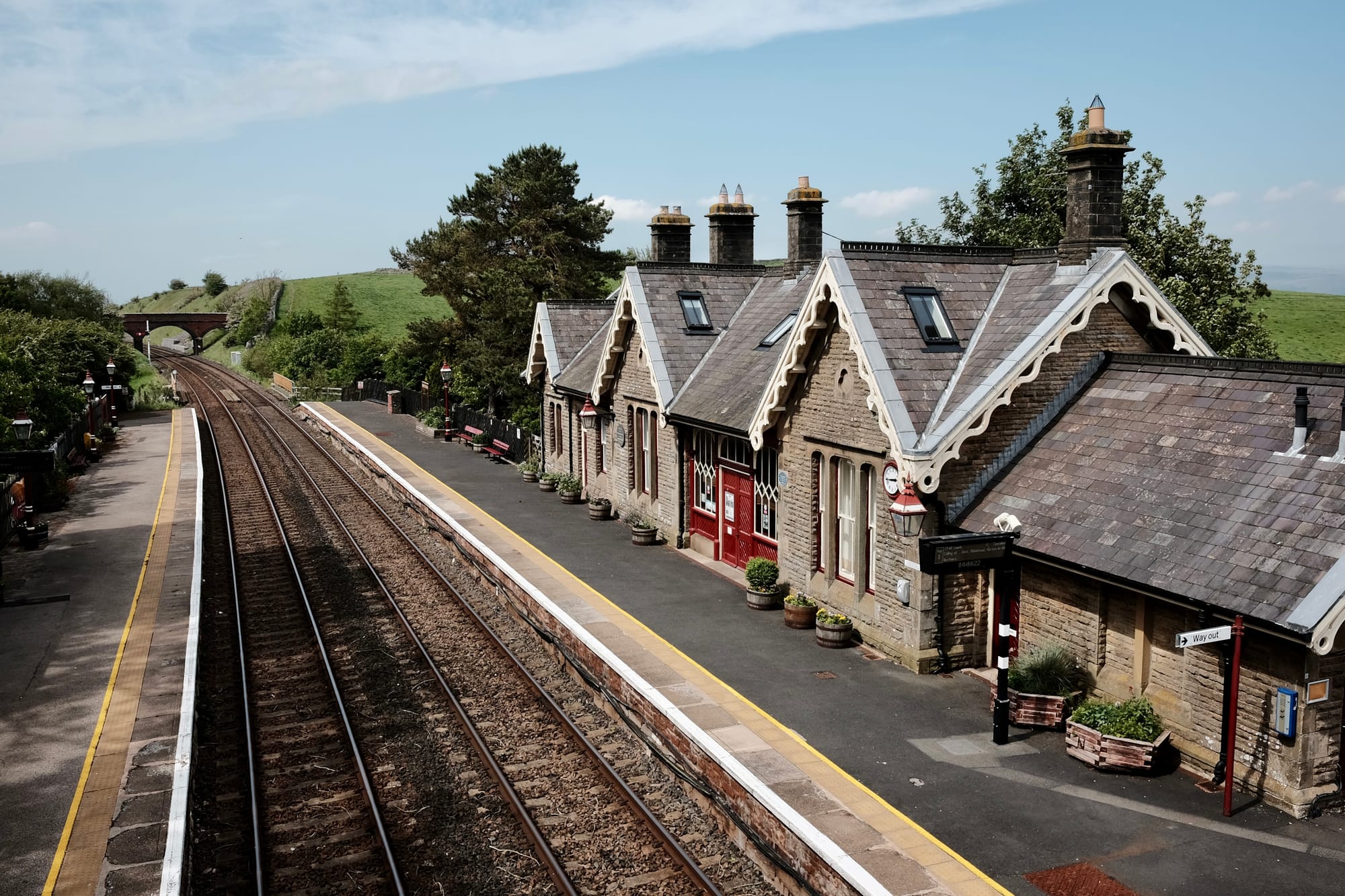 The stone buildings of Kirkby Stephen railway station with their bright red paintwork stand beside two empty train tracks.