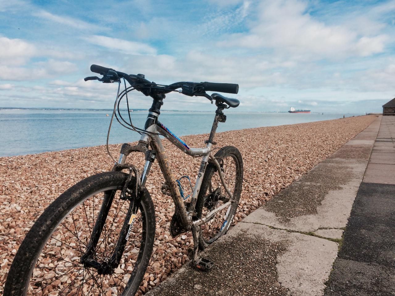 A mud-splattered mountain bike on the shingle beach at Cowes, Isle of Wight – with a ship in the background.