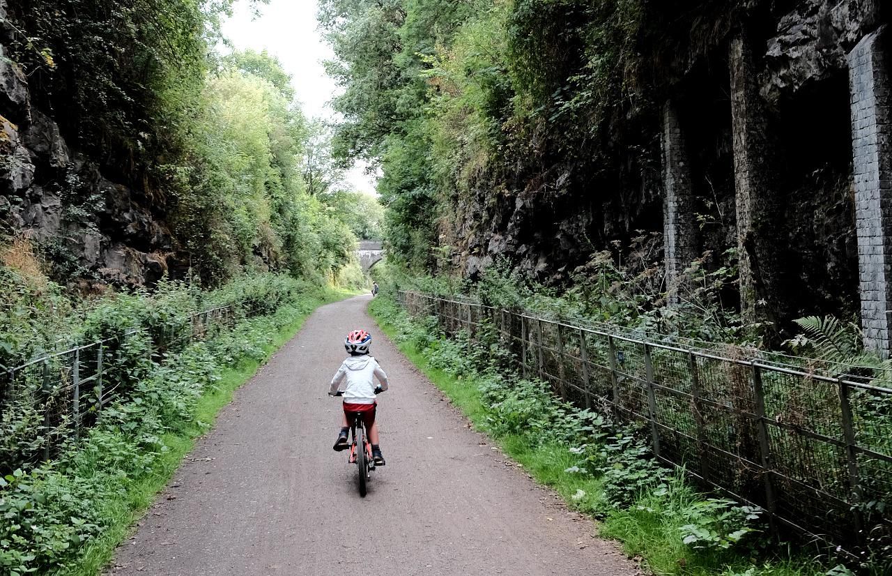 A child rides along a path in a deep rock cutting on the Monsal Trail.