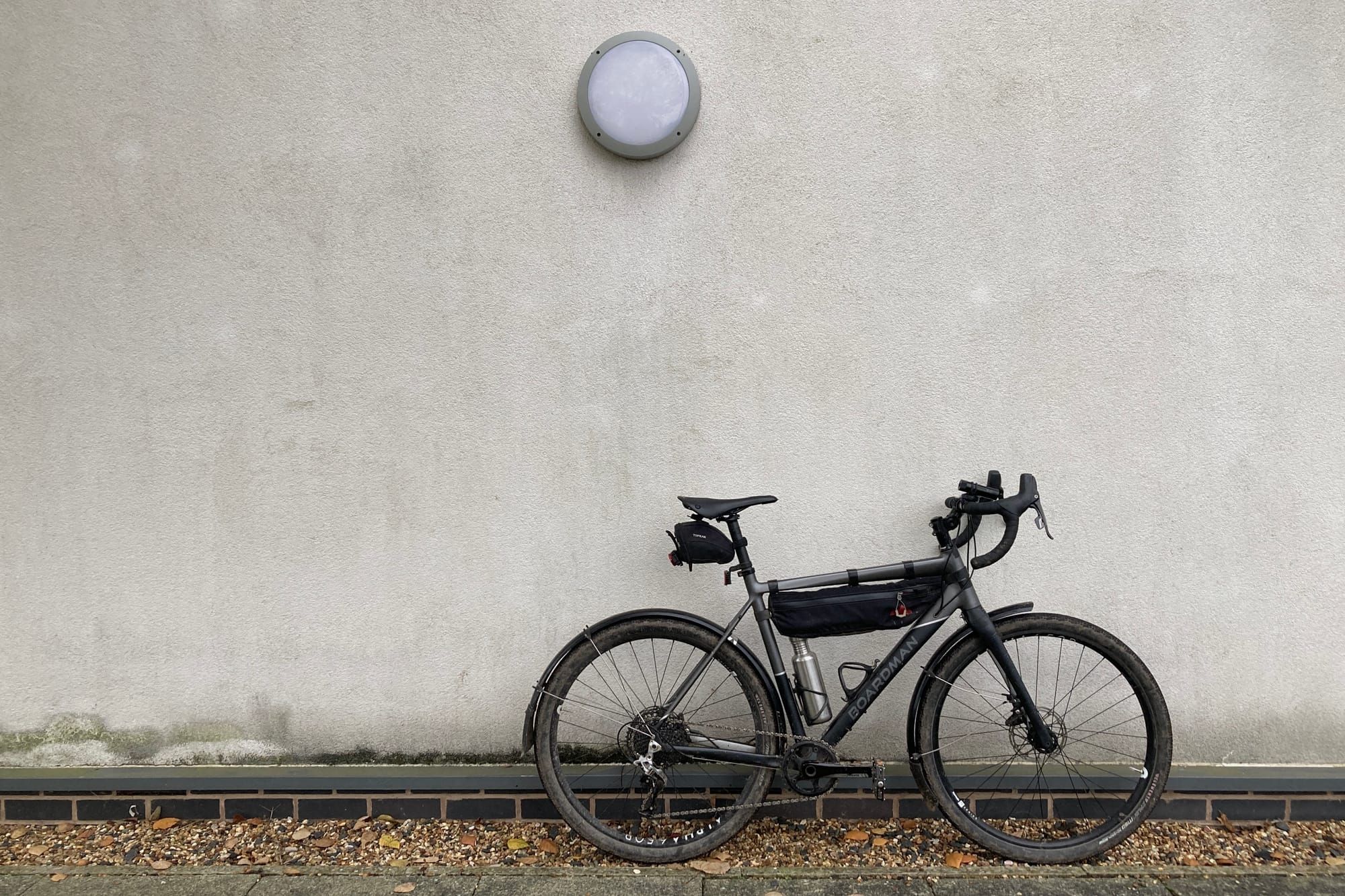 A black and grey gravel bike propped against a dirty white-rendered wall.