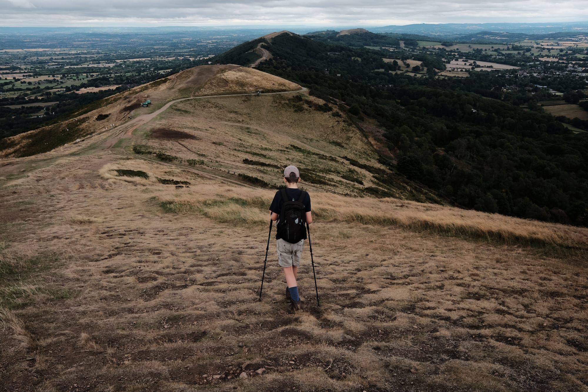 A child with walking poles descends a ridge on a yellow-grassed range of hills.