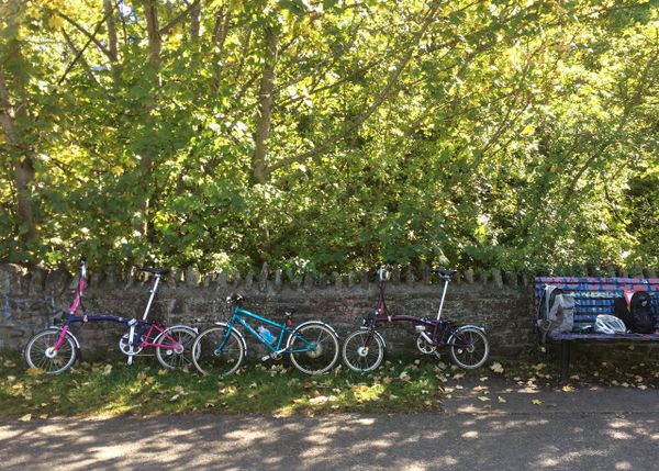 Two Brompton bikes and a child's Islabike lean against a wall on the Bristol-Bath cycle path.