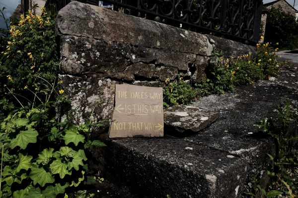 A notice in yellow chalk on a square brown stone reads "The Dales Way is this way (left) not that way (right)".