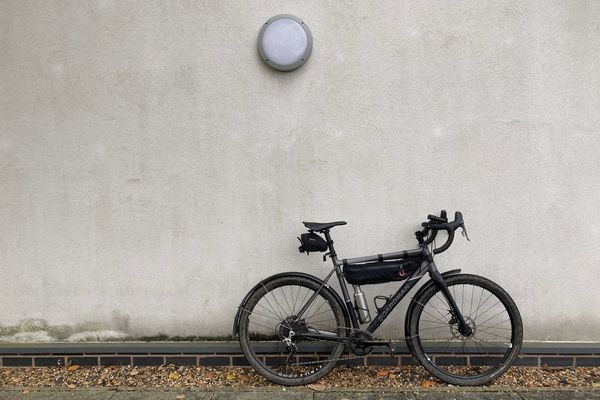 A black and grey gravel bike propped against a dirty white-rendered wall.