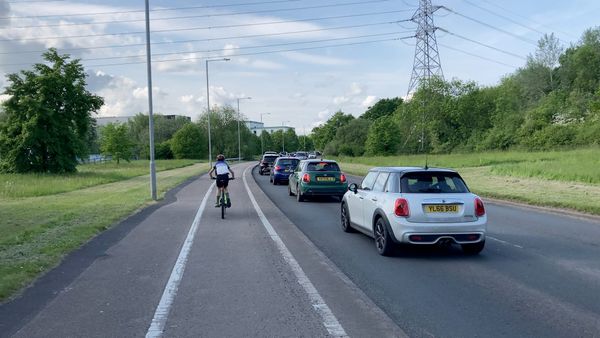 A child in a blue and white top rides a bike along a cycle path next to a traffic jam.