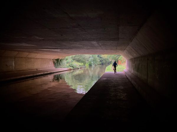 The silhouette of a cyclist riding along the canal towpath as it passes through a long tunnel.