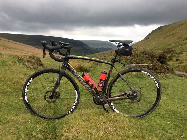 A black road bike with two red water bottles stands on the grass beside Gospel Pass, the Black Moutnains stretching away into the distance.