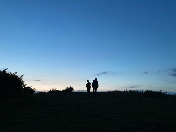 Two figures walking on a hillare silhouetted against the dark blue evening sky.