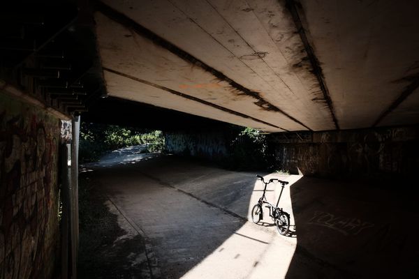A Brompton bike stands in a shaft of sunlight in a concrete underpass.