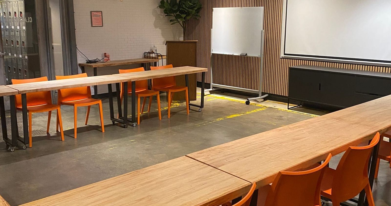 An empty classroom with rows of orange chairs facing a whiteboard and projector screen