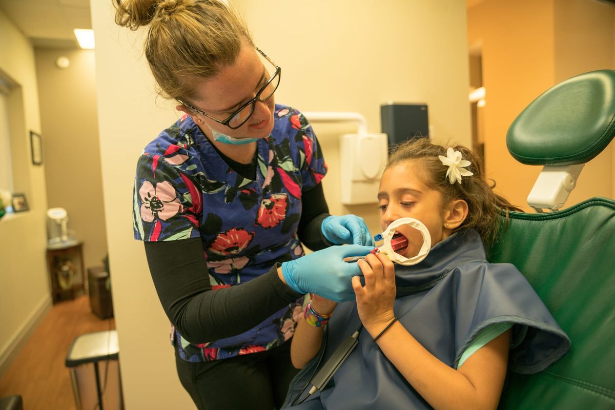 A young child sitting in a dental chair during a routine checkup, with a dental team member.