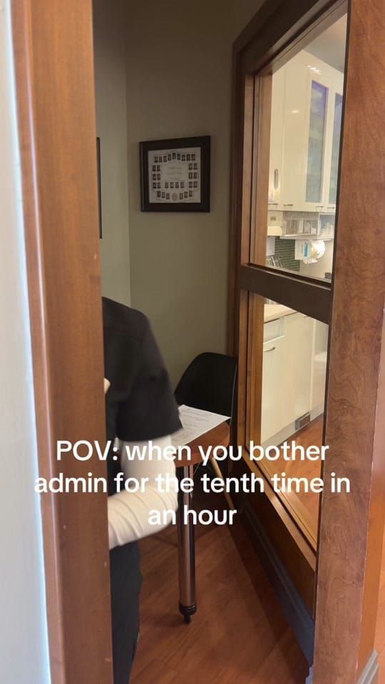 A view through a doorway into the Bowmanville admin office where a receptionist sits with paperwork, with on-screen text reading: POV: when you bother admin for the tenth time in an hour.
