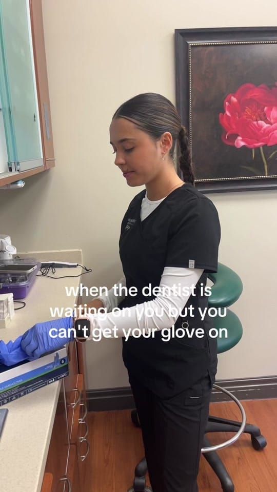 A Longworth Dental Bowmanville assistant pulling on a blue exam glove, with on-screen text reading: when the dentist is waiting on you but you can't get your glove on.