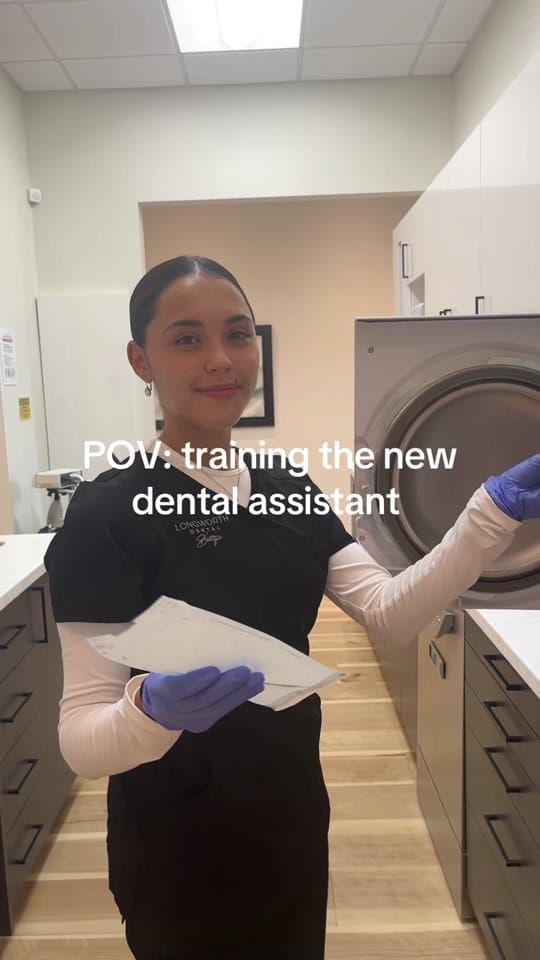 A Longworth Dental Courtice assistant in blue gloves at the sterilization autoclave holding pouches, with on-screen text reading: POV: training the new dental assistant.