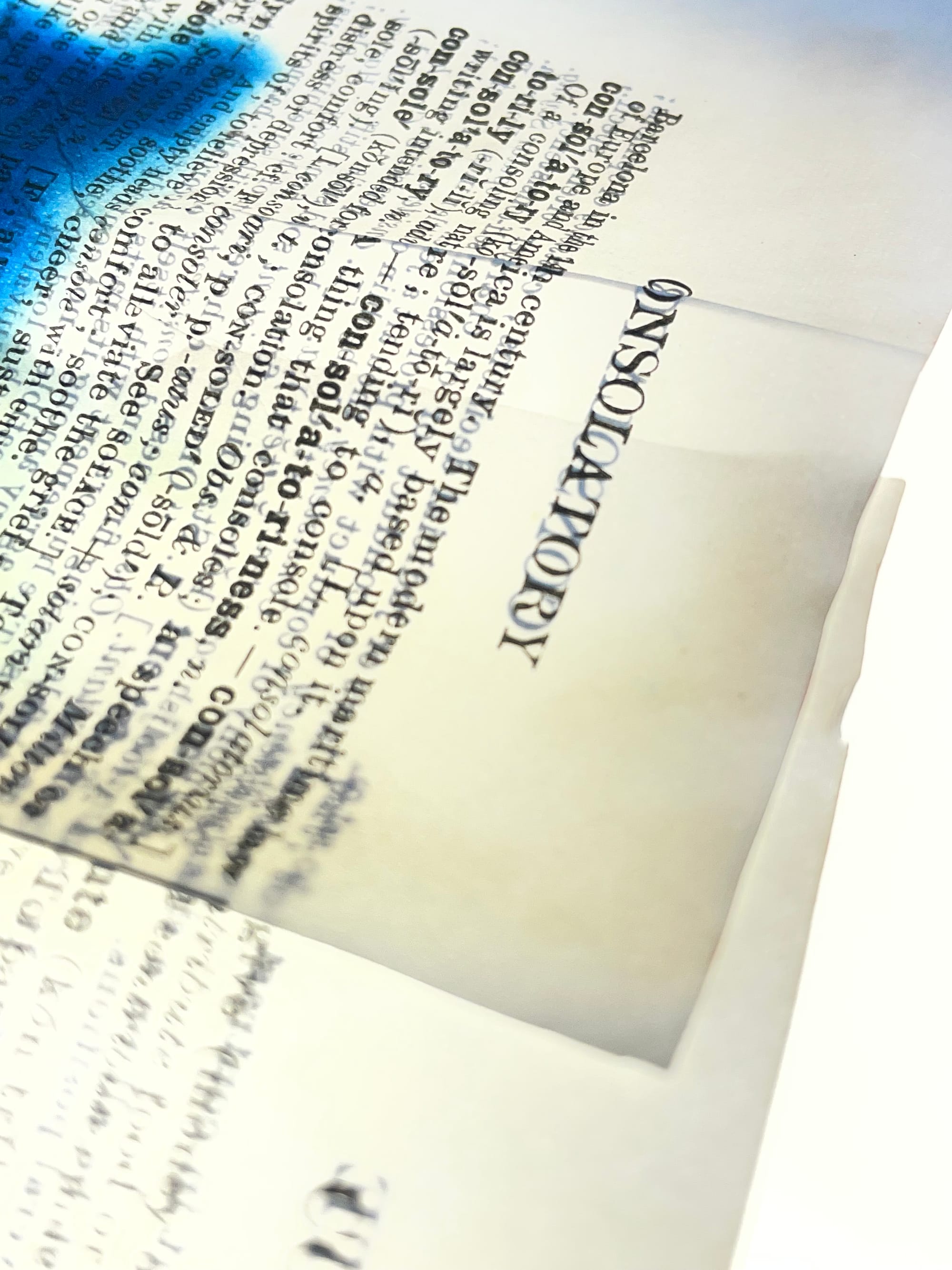 Close-up of layered translucent dictionary pages with blue pigment spreading across overlapping vintage text.