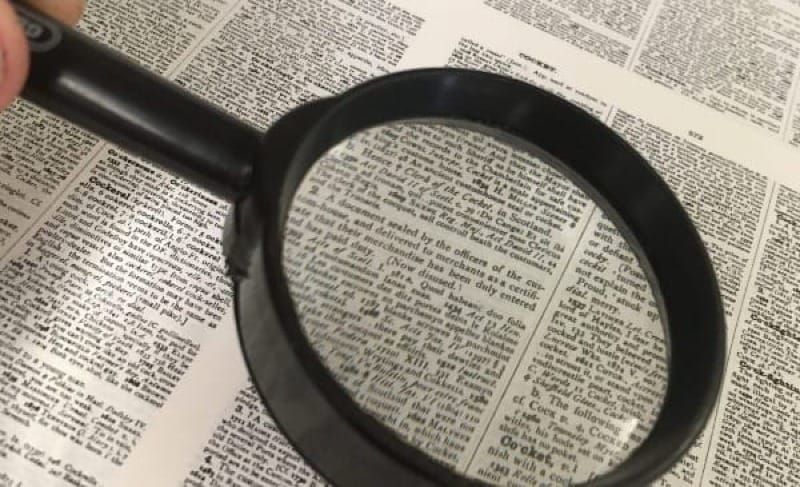 A magnifying glass is held with a dictionary page in the background.