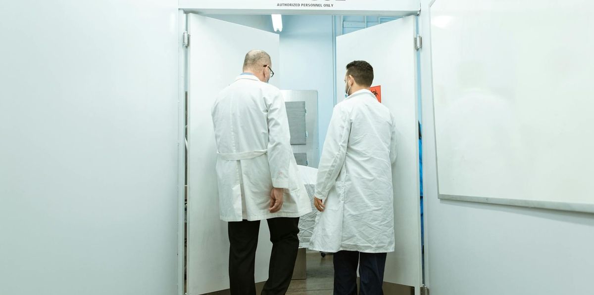 Medical professionals in lab coats entering a morgue with a body on stretcher.