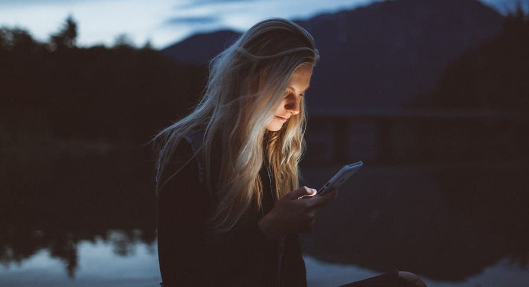 woman looking at phone beside body of water
