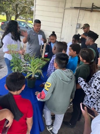 A group of children standing around a table with plants

AI-generated content may be incorrect.