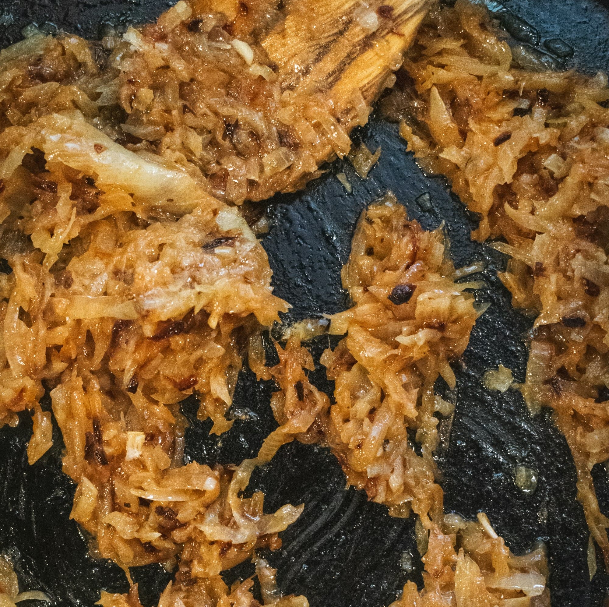a frying pan filled with fried food and a wooden spoon