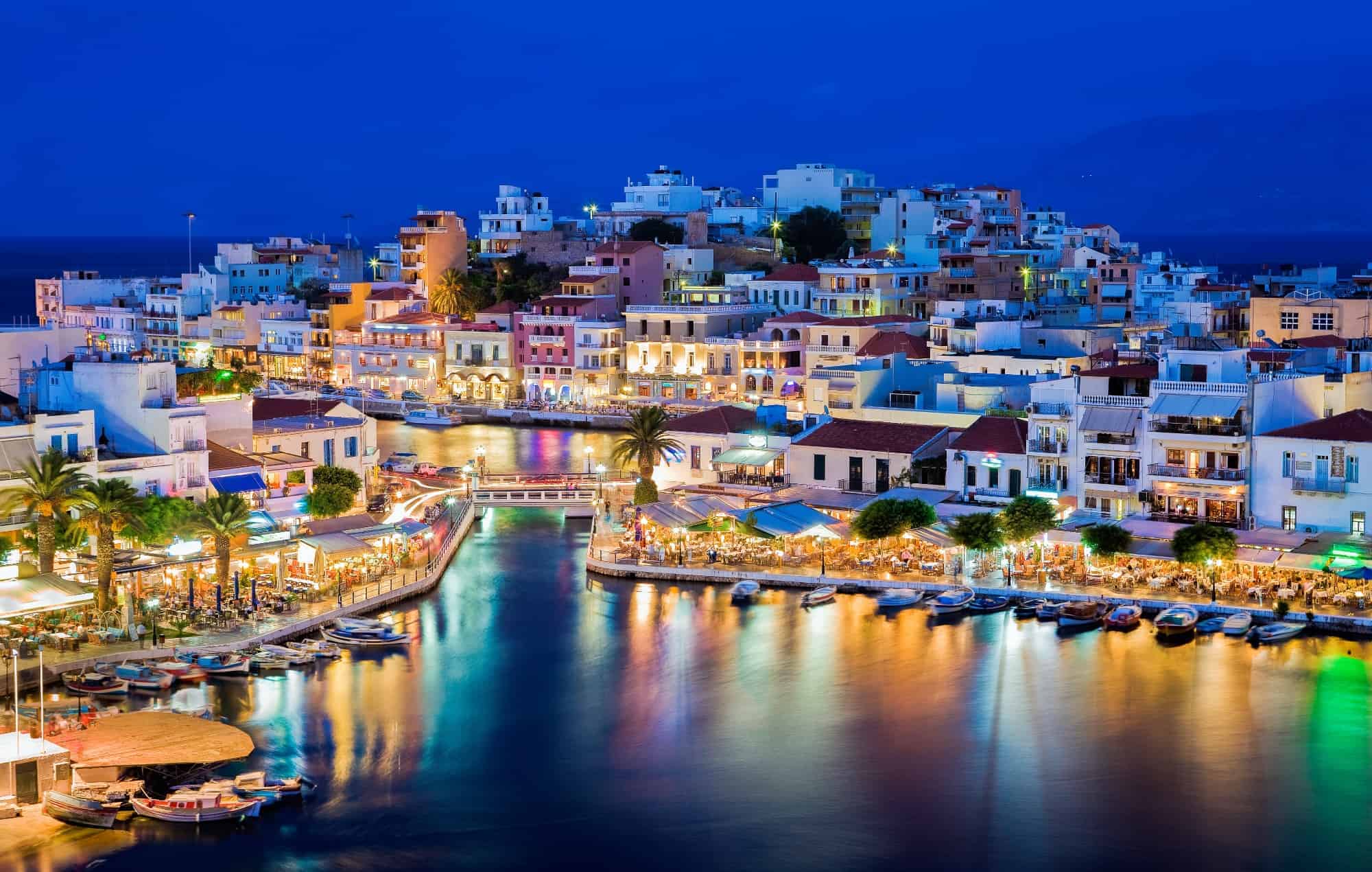 A harbor in Crete at night with colorful houses and lights reflected in the water