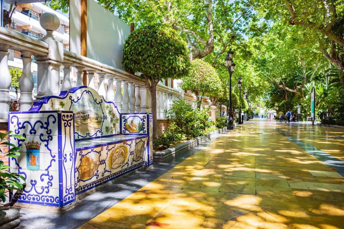 The Alameda Park of Marbella on a sunny day - tiled paths shaded by lush tall trees.