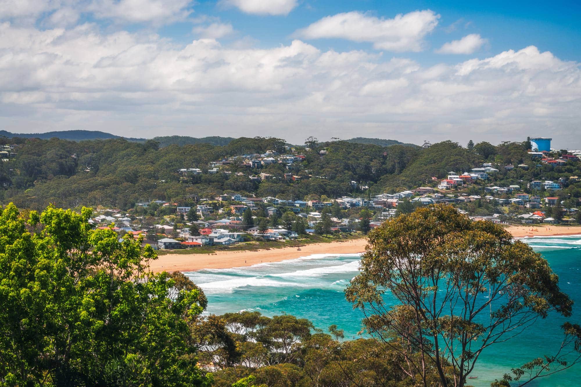 Avoca Beach on the Central Coast, New South Wales. A sandy beach, green hills and family homes among trees. 