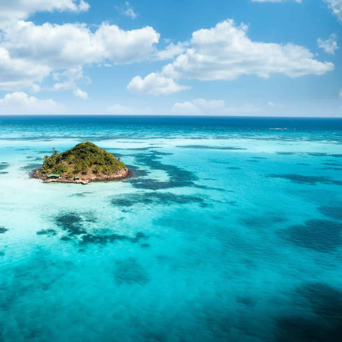 A stunning aerial view of Cayo Cangrejo, a small, lush green island surrounded by the vibrant turquoise waters of the Caribbean Sea near Providencia, Colombia. 