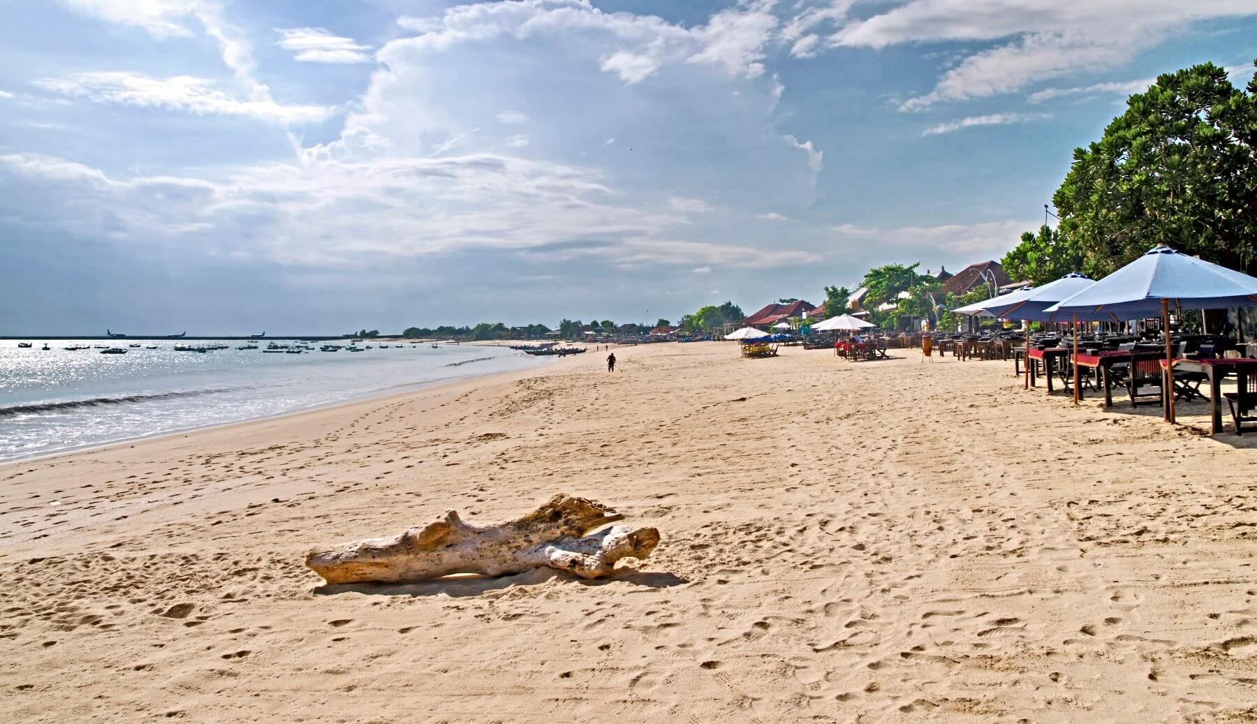 A long stretch of a sandy beach, blue sky and beach huts - Bali