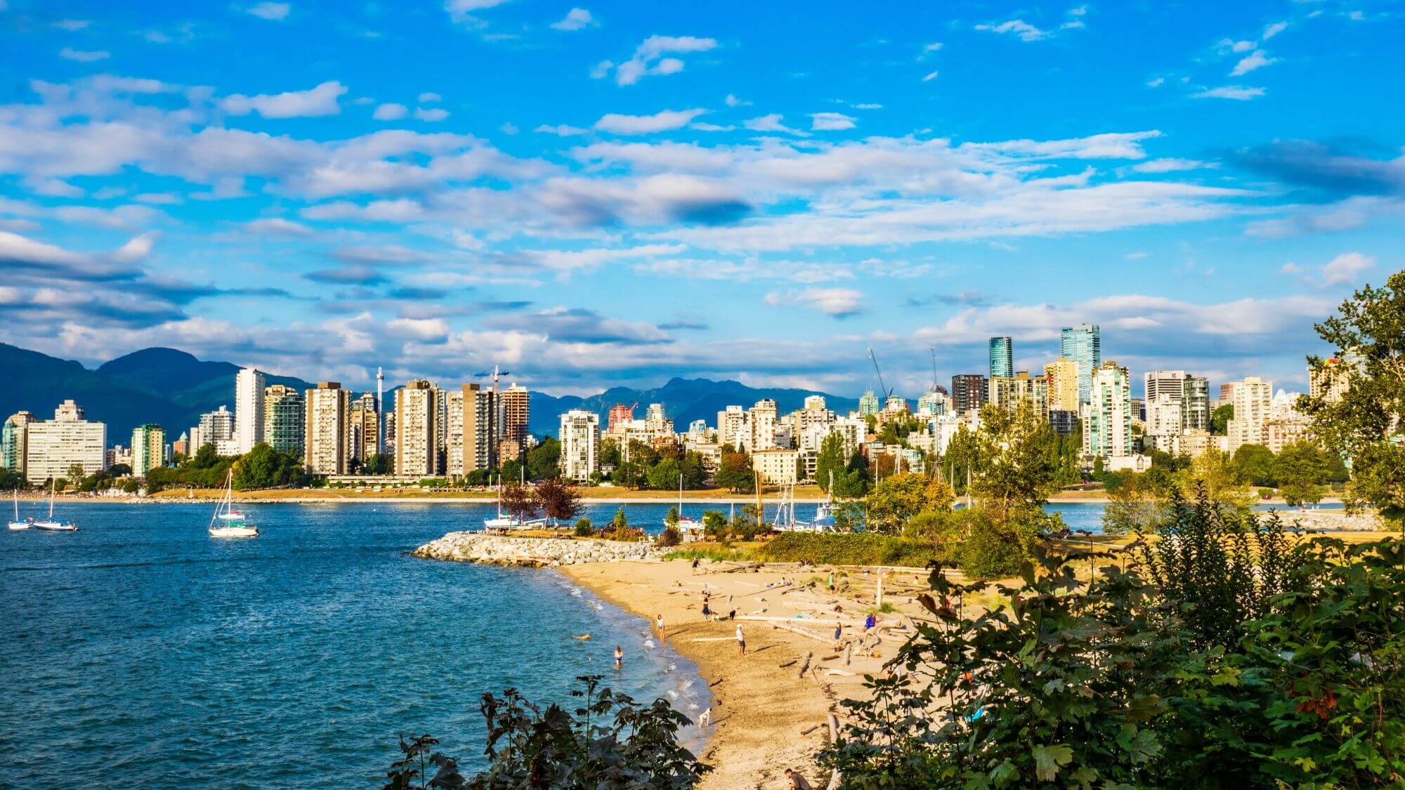 A sandy shore and a cityscape of Vancouver across the water of the Kitsilano Beach
