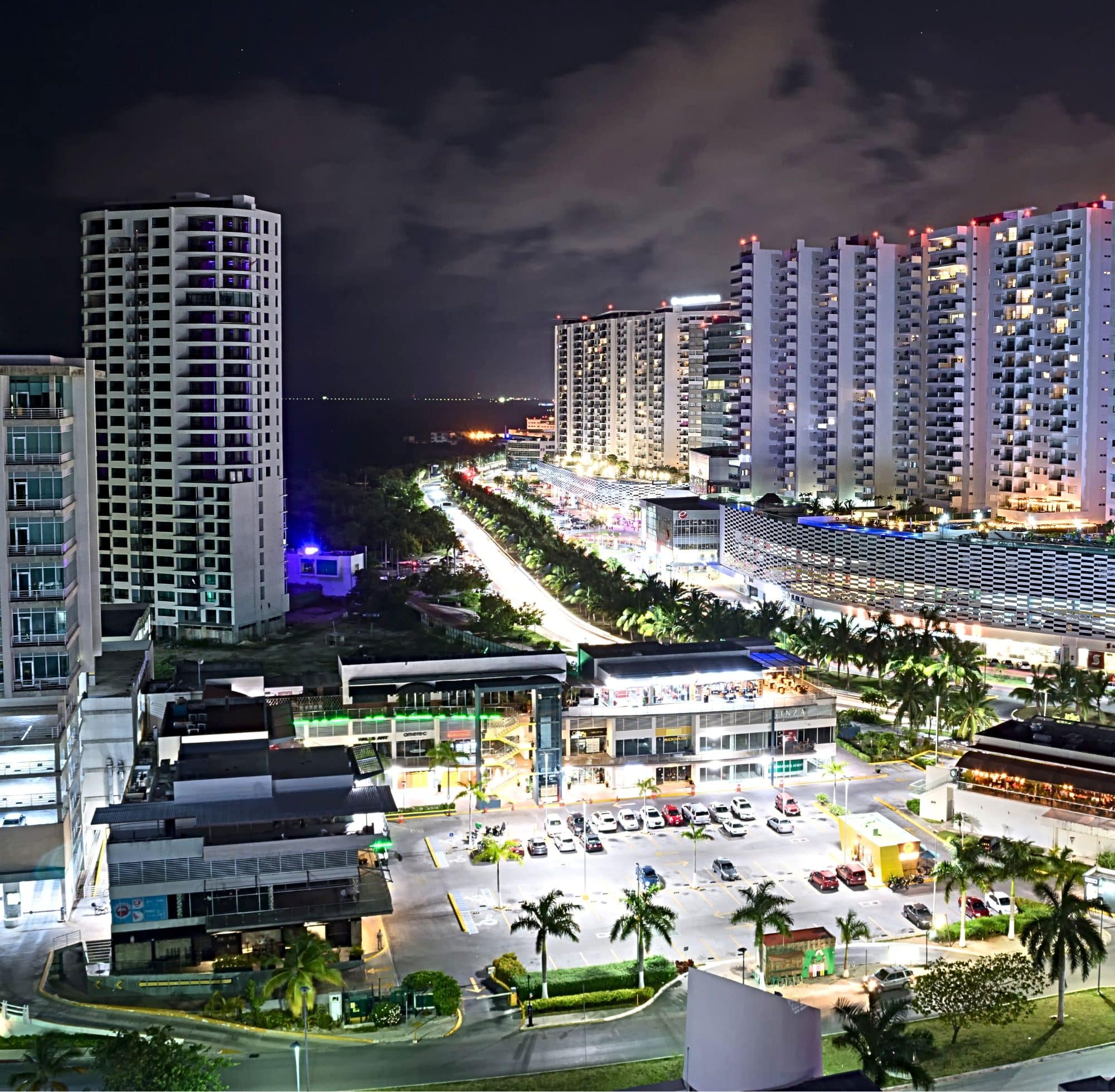 A night view of Plaza Las Americas in downtown Cancun, bright street lights lighting up the plaza and high rise residential buildings 