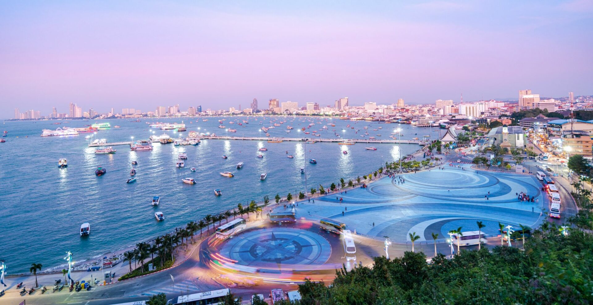 A coastal city of Pattaya at sunset - pink sky and city lights reflecting in the bay