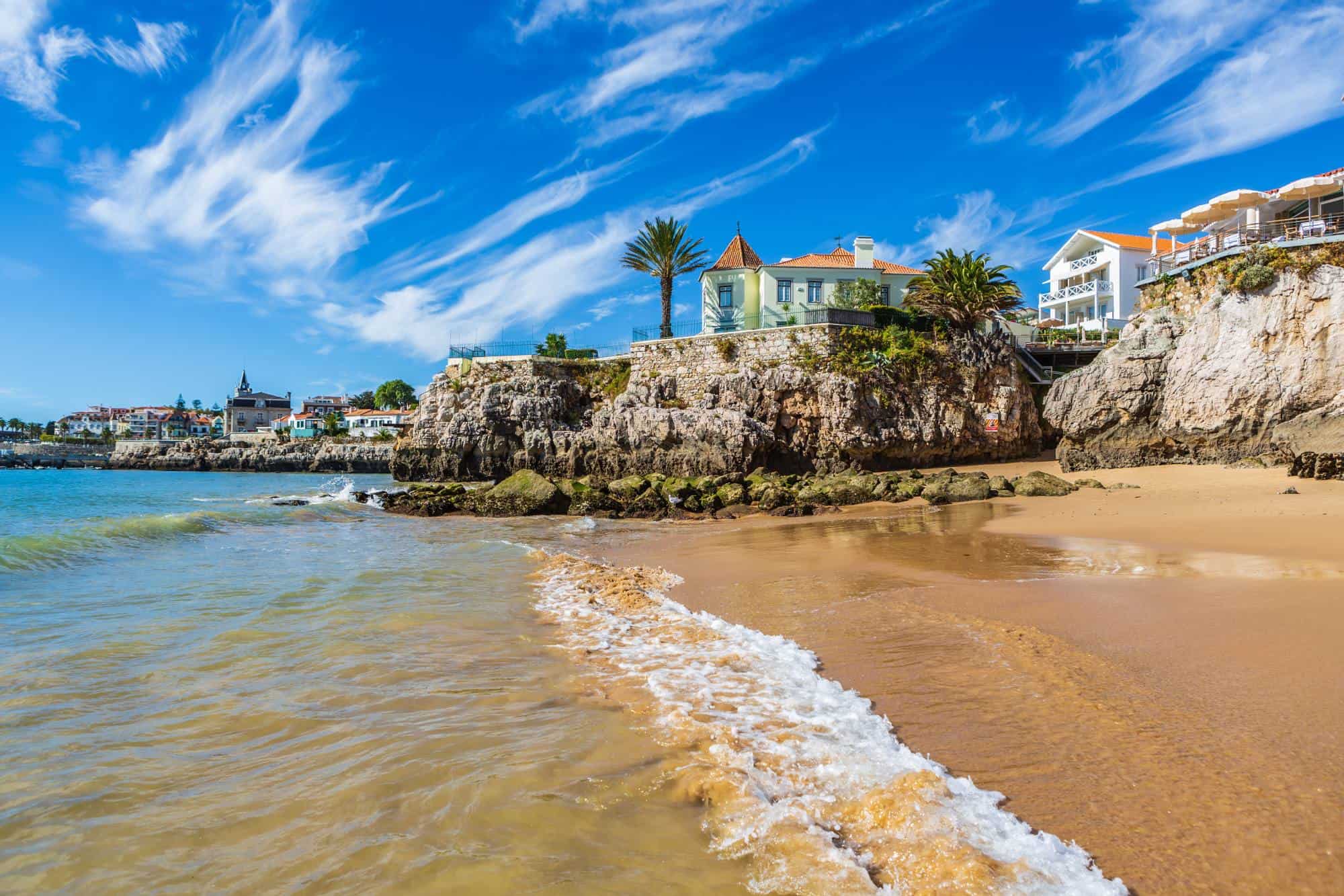 A long stretch of a sandy beach along the rocky coast with houses along the coast. 