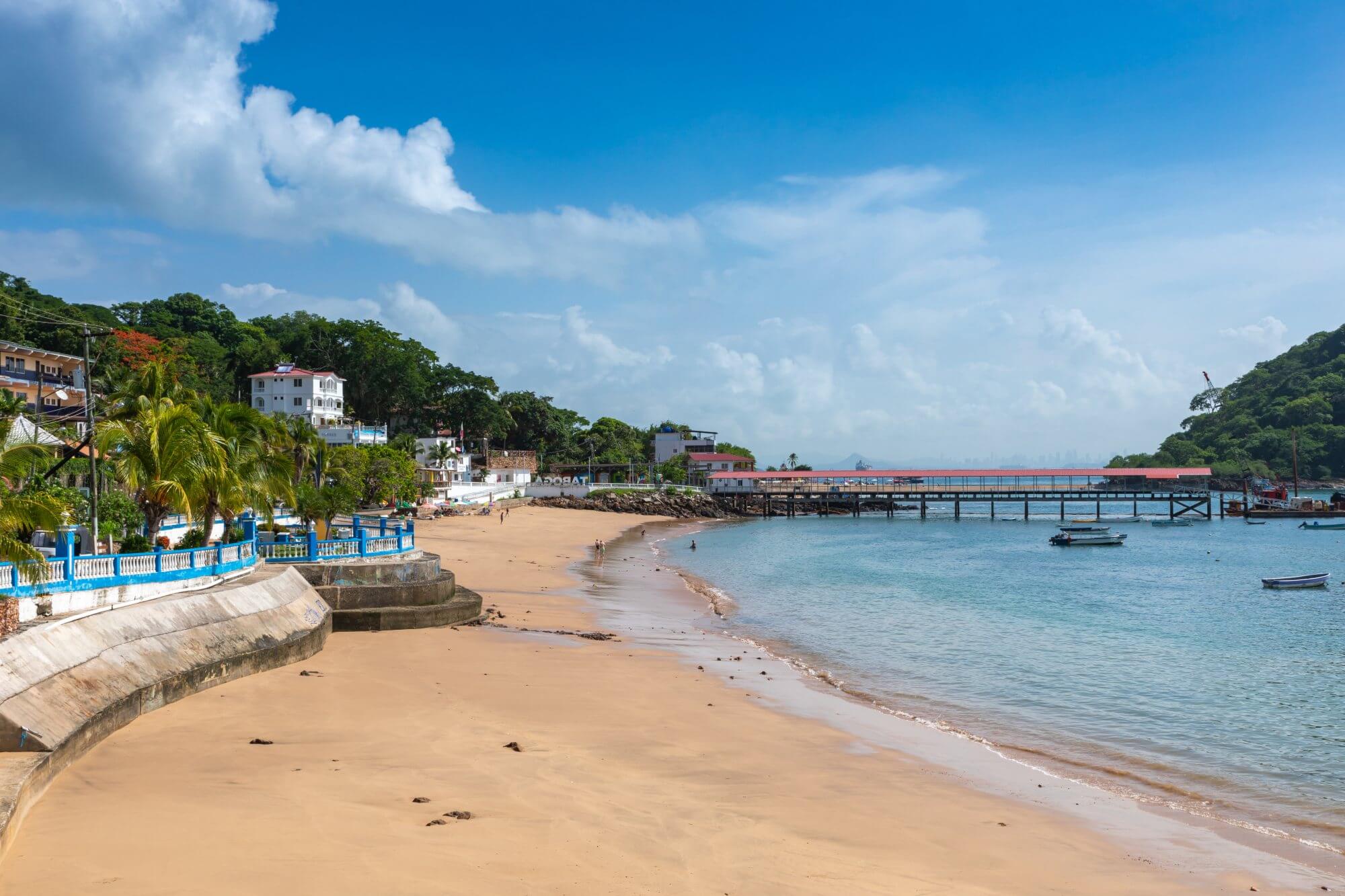 A long sandy beach on Taboga Island, Panama with beach side houses and tropical greenery