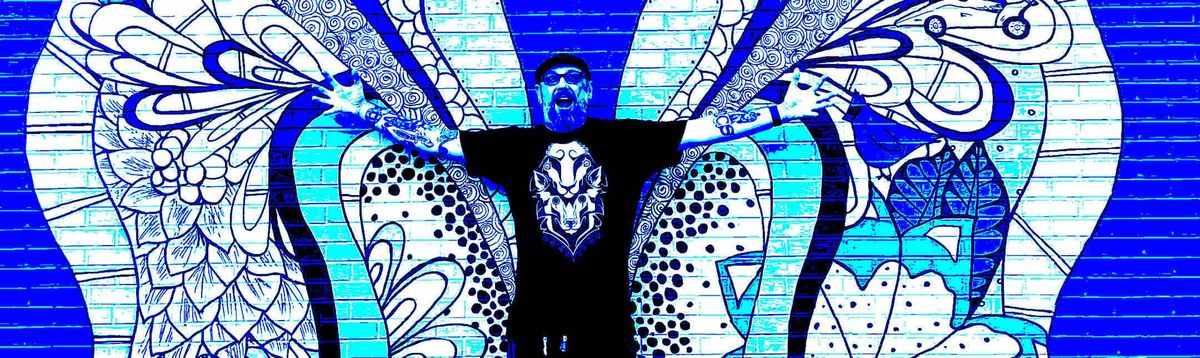 A man standing in front of a mural, arms out stretched, face in a scowl