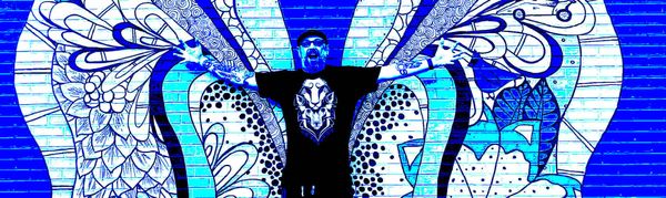 A man standing in front of a mural, arms out stretched, face in a scowl