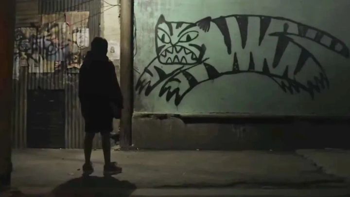 A little boy stares at a graffiti'd tiger on a wall. 